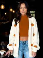 Woman wearing a white cardigan with pumpkin patterns in a casual setting.
