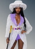 Woman in a white fringed outfit with a purple top and shorts, holding a cane against a gray background.