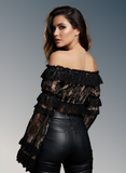 Woman wearing a black off-shoulder top and leather pants against a gray background