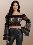 Woman wearing a black lace top and black pants against a beige background